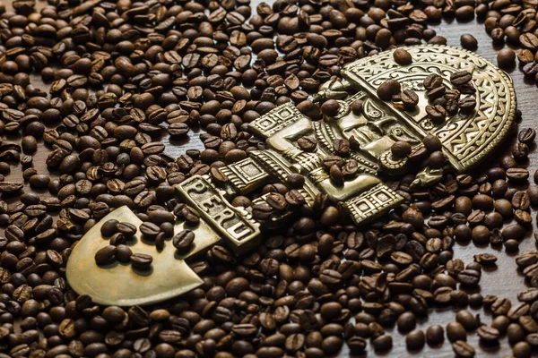 Coffee spills out of the bag onto the table. Arabica and robusta on a dark wood table. Brown color. Coffee beans scattered on the surface. Place for the text. God of Peru. Peruvian god statuette