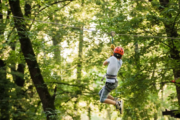 El niño pequeño supera el obstáculo en el parque de cuerdas. Escalada en curso de cuerda alta disfrutando de la aventura. Aventura escalada bosque de alambre alto - personas en curso en casco de montaña y equipo de seguridad. Imagen de stock