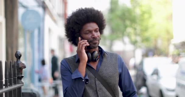 Hombre afroamericano caminando y encendido en smartphone en la ciudad — Vídeo de stock