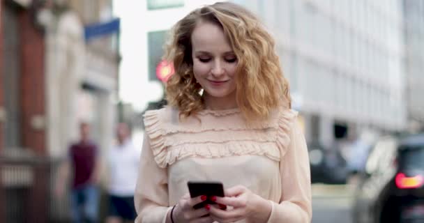 Jonge volwassen vrouwtje kijken naar smartphone buitenshuis in stad — Stockvideo