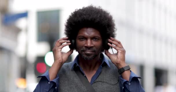 Retrato de afro-americano masculino ao ar livre na cidade ouvindo fones de ouvido — Vídeo de Stock