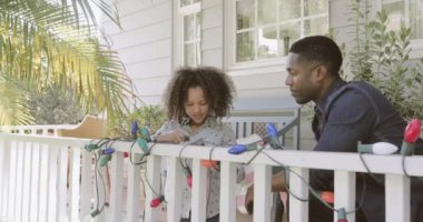Afro-Amerikan baba ve kız açık havada Noel ışıkları yakmaya