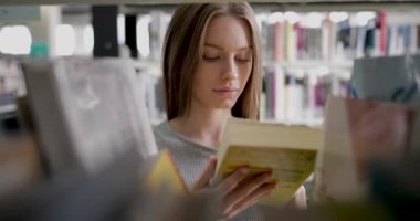Genç kız kütüphanede kitap seçimi