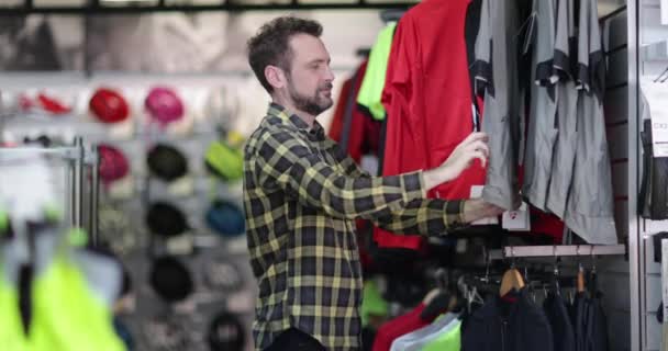 Дорослий чоловік дивиться на спортивний одяг в магазині — стокове відео
