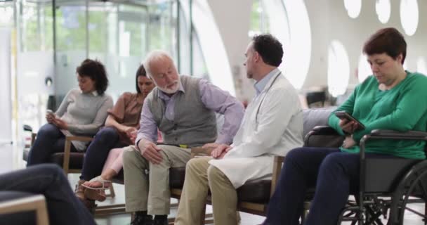 Sénior Masculino conversando com o Doutor em uma sala de espera lotada do hospital — Vídeo de Stock