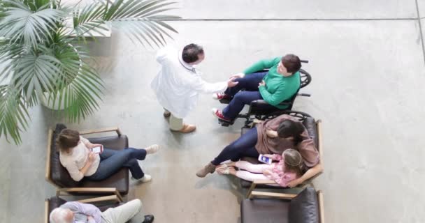 Overhead shot of Medical Doctor greeting woman in wheelchair in waiting room — Stock Video