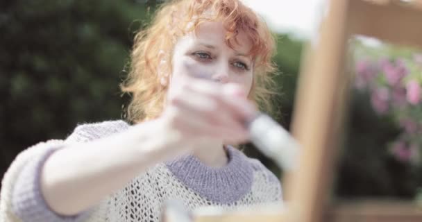 Rood haar vrouw schilderen stoel in de tuin op een zomerse dag — Stockvideo