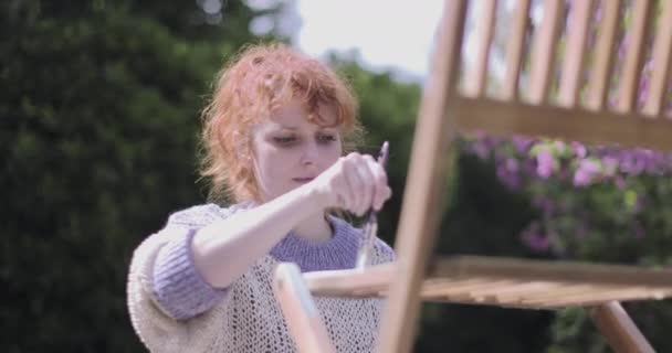 Young Adult woman painting chair in garden on a summer day — 비디오