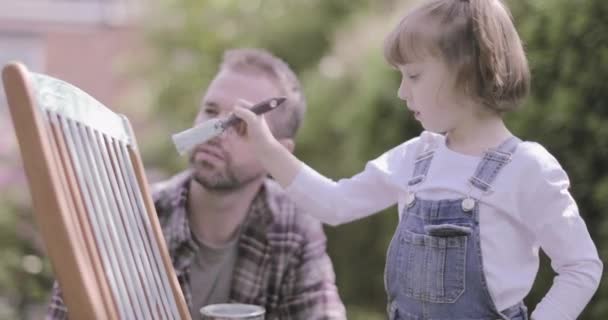 Father painting chair with daughter in garden — 비디오