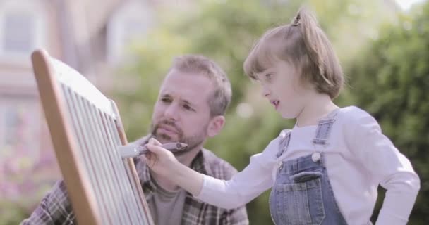 Father painting chair with daughter in garden — 비디오