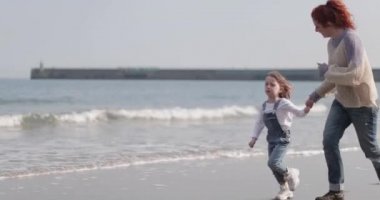 Anne ve çocuk sonbaharda plajda koşuyorlar.