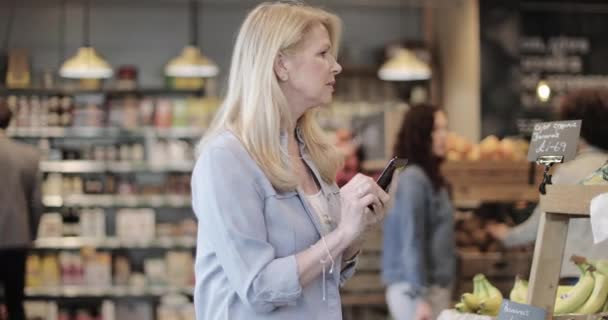 Senior vrouw doet wekelijkse kruidenierswinkel met behulp van smartphone — Stockvideo