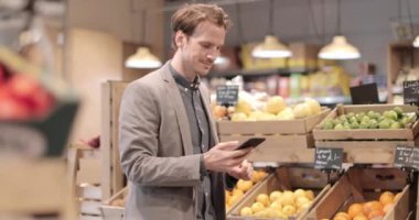 Yetişkin erkek gece yarısı market alışverişi yapıyor ve akıllı telefon kullanıyor.
