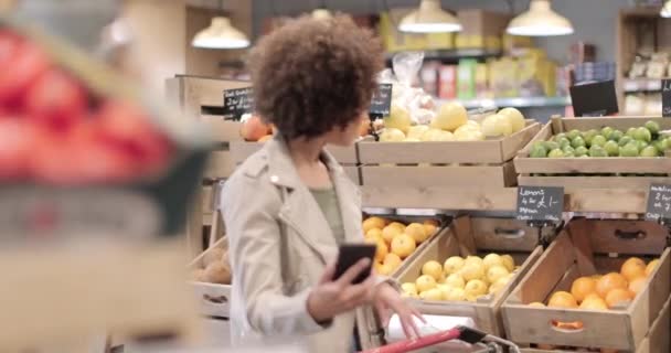 African American female grocery shopping and using smartphone — 비디오