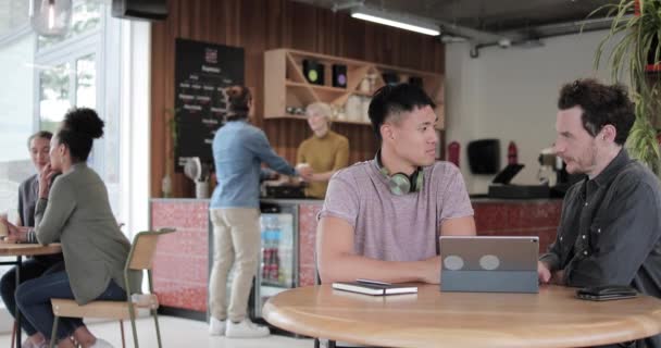 Ελεύθεροι επαγγελματίες σε μια συνάντηση σε ένα καφέ κοιτάζοντας μια ψηφιακή ταμπλέτα — Αρχείο Βίντεο