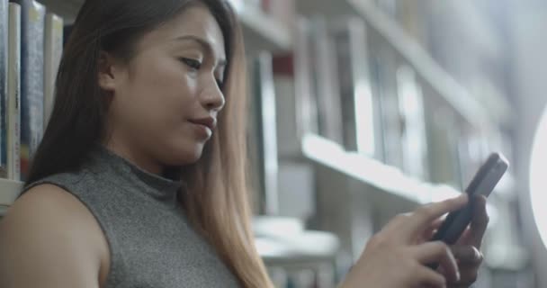 Asiatisk kvinna studerar i Universitetsbiblioteket och tittar på vän medan textning — Stockvideo