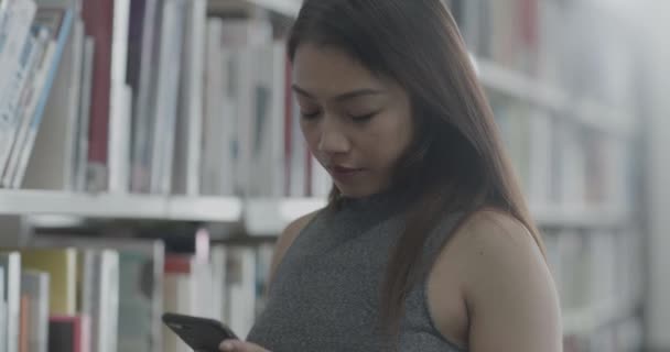 Asiática mujer estudiando en la biblioteca universitaria y recibiendo mensaje en el teléfono inteligente — Vídeos de Stock