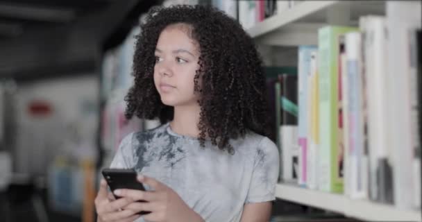 Portret van Afrikaanse Amerikaanse middelbare school student in de bibliotheek met behulp van smartphone — Stockvideo