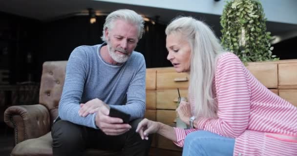 Couple de personnes âgées dans le salon de luxe de l'hôtel partageant des photos sur téléphone intelligent — Video