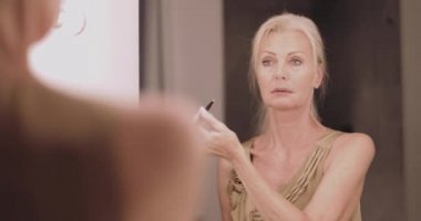 Yetişkin bir kadın aynada makyaj yapıyor ve giyiniyor.