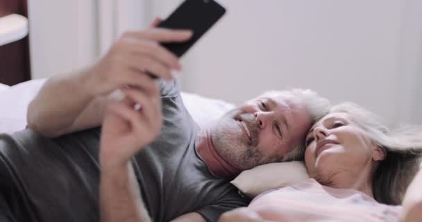 Idős felnőtt pár nyaralni csinál selfie a hotel hálószobájában — Stock videók