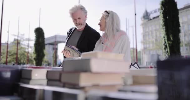 Pareja adulta mayor de vacaciones mirando libros en el mercado de pulgas al aire libre — Vídeos de Stock