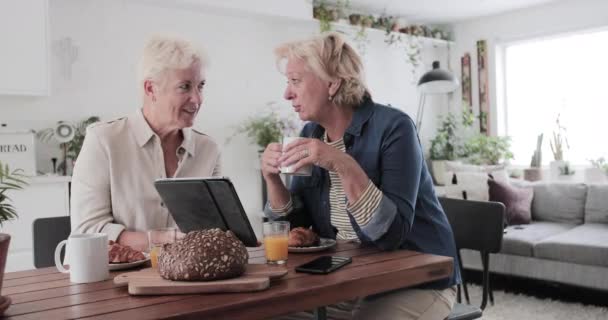 Mature lesbian couple looking at digital tablet at breakfast — 비디오