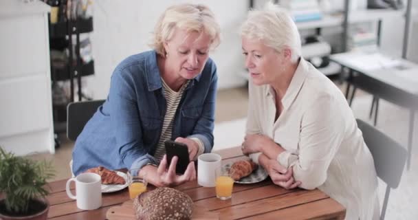 Mature lesbian couple looking at a smartphone at breakfast — 비디오