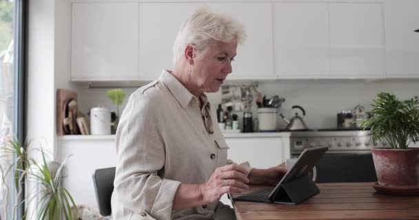 Volwassen volwassen vrouw in de keuken met behulp van een digitale tablet met toetsenbord — Stockvideo