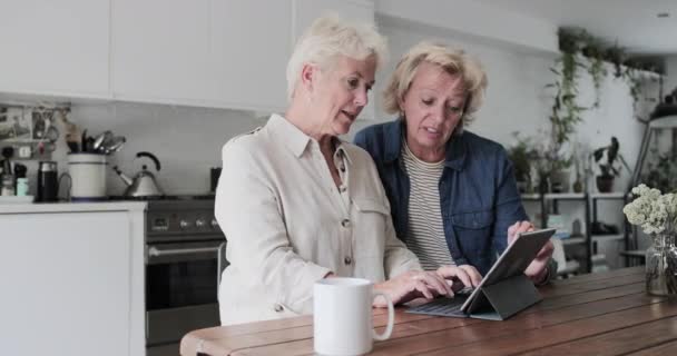 Mature lesbian couple looking at digital tablet together at home — 图库视频影像