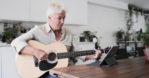 Volwassen volwassen vrouw leren om de gitaar te spelen thuis met een video tutorial — Stockvideo