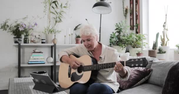 Gammal vuxen kvinna lära sig att spela gitarr hemma med en video tutorial — Stockvideo