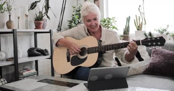 Ώριμη ενήλικη γυναίκα μαθαίνει να παίζει κιθάρα στο σπίτι με ένα βίντεο φροντιστήριο — Αρχείο Βίντεο