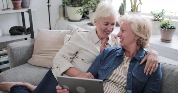 Mature lesbian couple looking at digital tablet together on sofa — ストック動画