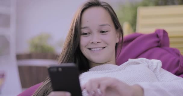 Joven mujer adulta sentada afuera usando un teléfono inteligente — Vídeos de Stock