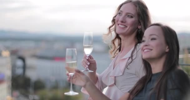 Two women in cocktail dress celebrating and toasting on roof terrace in city — Stock Video