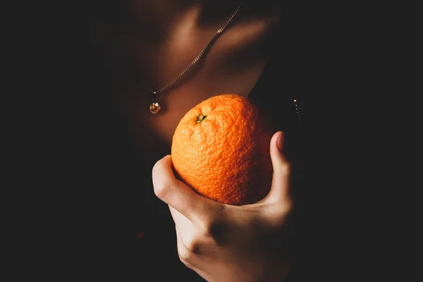 The girl holds an orange in her hand. Orange on a dark background