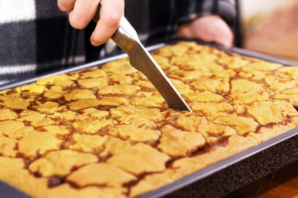 The hand is cutting the cake. Cake on a baking sheet