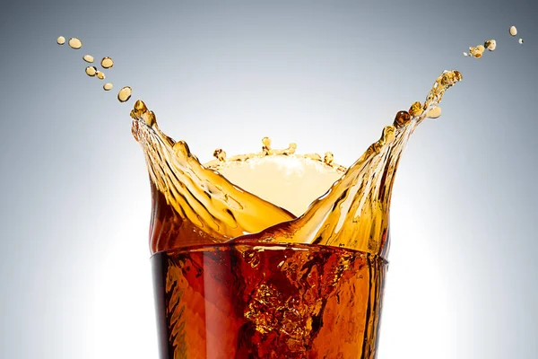 Big splash in a glass filled with Cola isolated on light grey background with halo. High speed beverage photography, closeup
