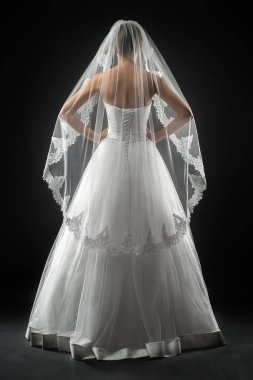 Şık, beyaz bir gelinlik ve uzun dantelli bir duvak giyen gelin. Siyah arkaplan