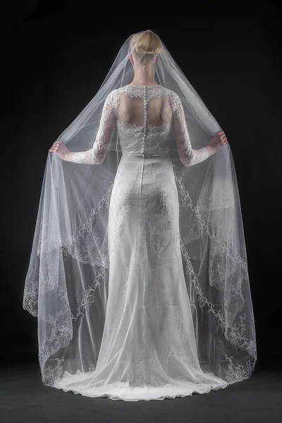 Şık, beyaz bir gelinlik ve uzun dantelli bir duvak giyen gelin. Siyah arkaplan