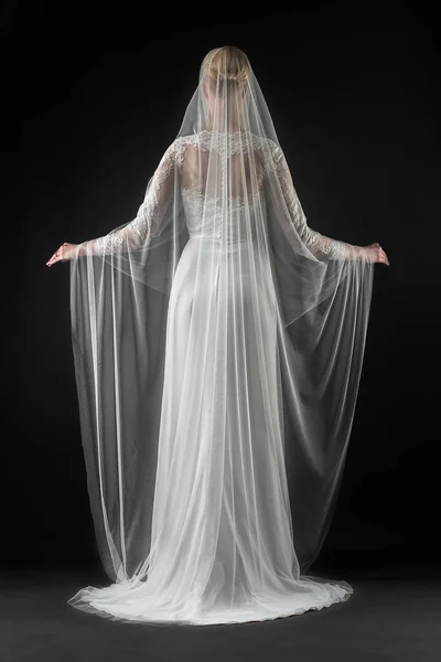 Şık, beyaz bir gelinlik ve uzun dantelli bir duvak giyen gelin. Siyah arkaplan