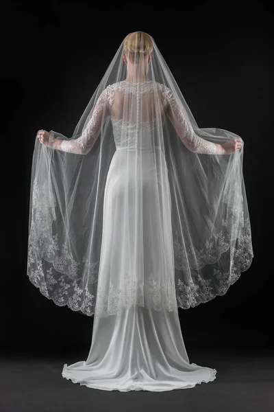 Şık, beyaz bir gelinlik ve uzun dantelli bir duvak giyen gelin. Siyah arkaplan