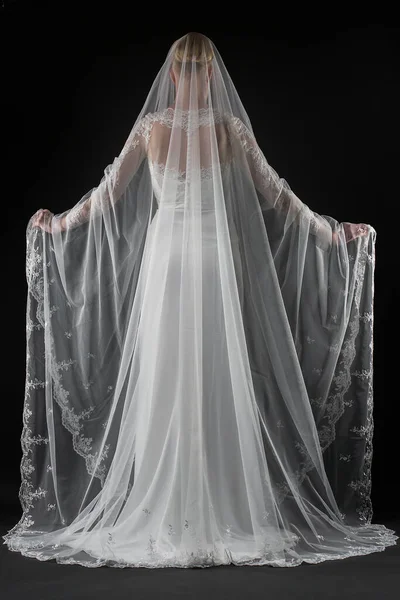 Şık, beyaz bir gelinlik ve uzun dantelli bir duvak giyen gelin. Siyah arkaplan