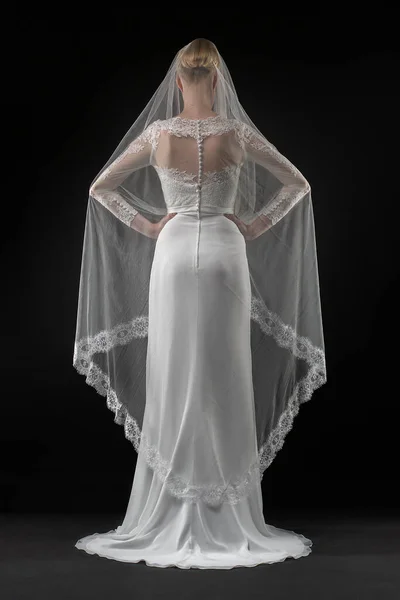 Şık, beyaz bir gelinlik ve uzun dantelli bir duvak giyen gelin. Siyah arkaplan