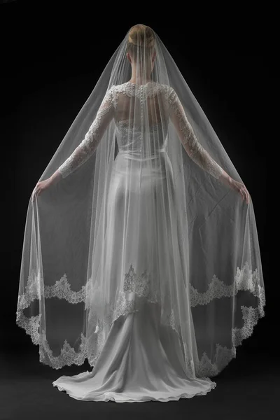 Şık, beyaz bir gelinlik ve uzun dantelli bir duvak giyen gelin. Siyah arkaplan