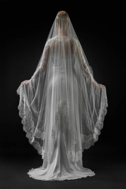 Şık, beyaz bir gelinlik ve uzun dantelli bir duvak giyen gelin. Siyah arkaplan