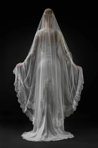 Şık, beyaz bir gelinlik ve uzun dantelli bir duvak giyen gelin. Siyah arkaplan