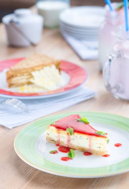 Renkli bir tabak ve ahşap masa üzerinde iki parça kek. Kırmızı jöleli ve naneli cheesecake. Arka plan bulanık. Sıcak restoran sahnesi