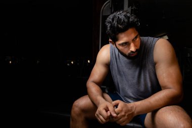 Asyalı yorgun adam spor salonunda antrenmandan sonra masada oturuyor.